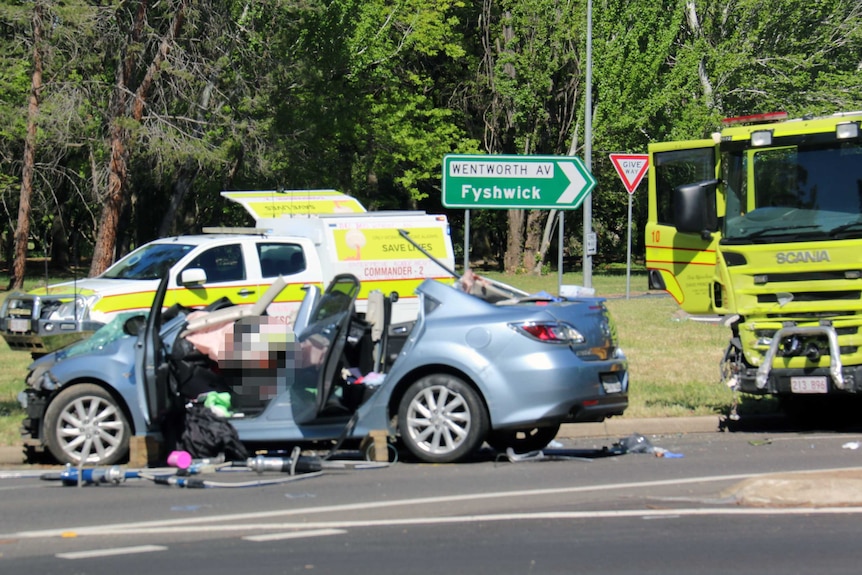 A broken car with smashed windows and chassis near a damaged fire truck.