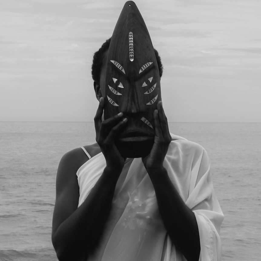 woman holds Solomon Island mask to cover face