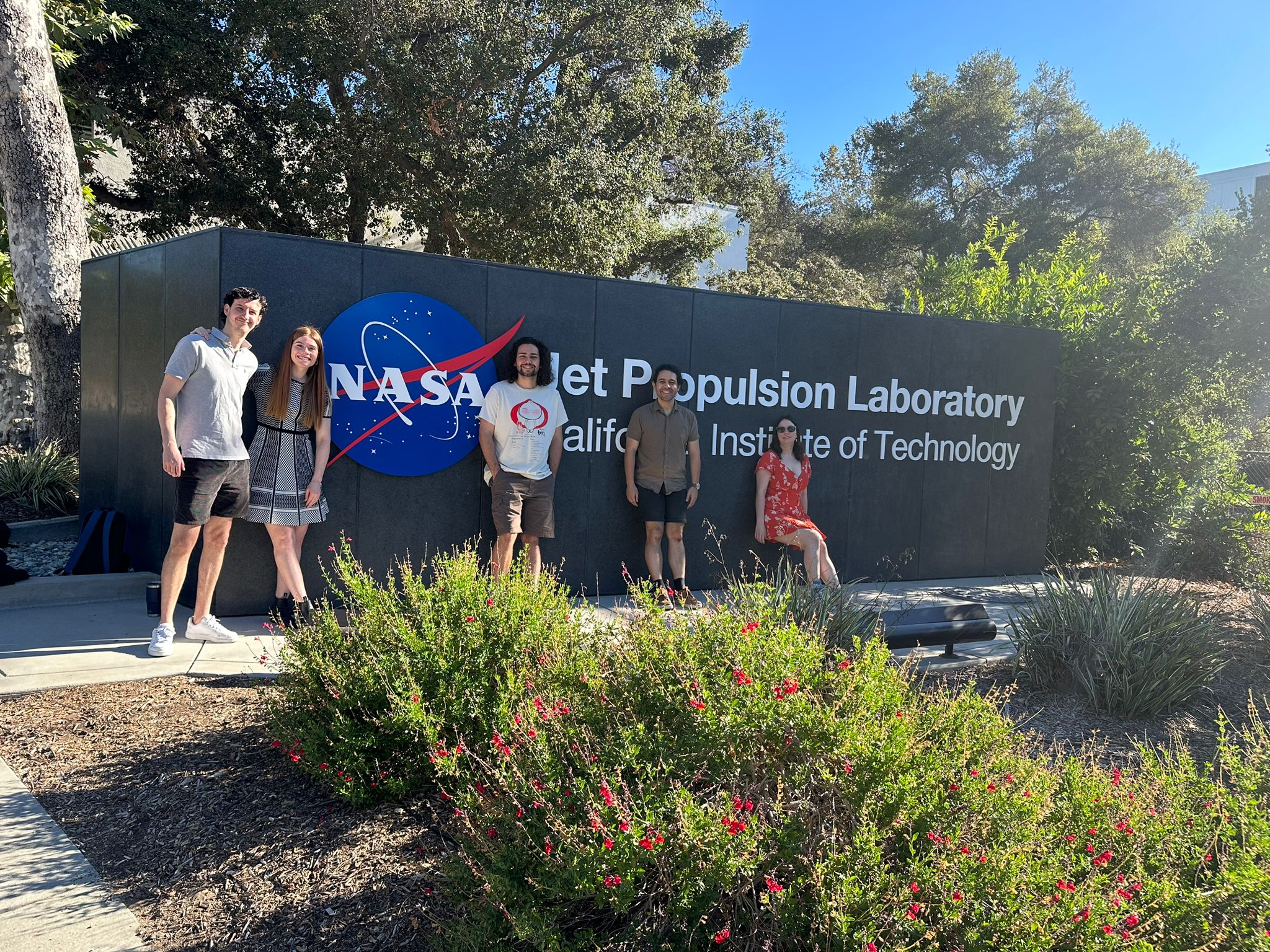 A group of students stand in front of a NASA sign smiling. 