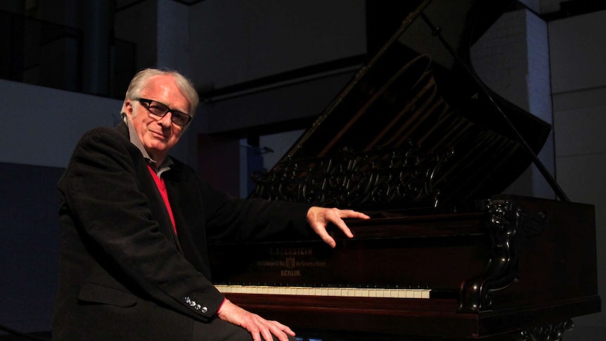 A man sits at a piano and smiles for the camera.