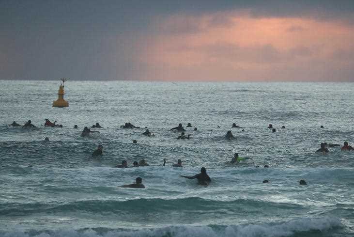 Dozens of surfers paddle out at dawn