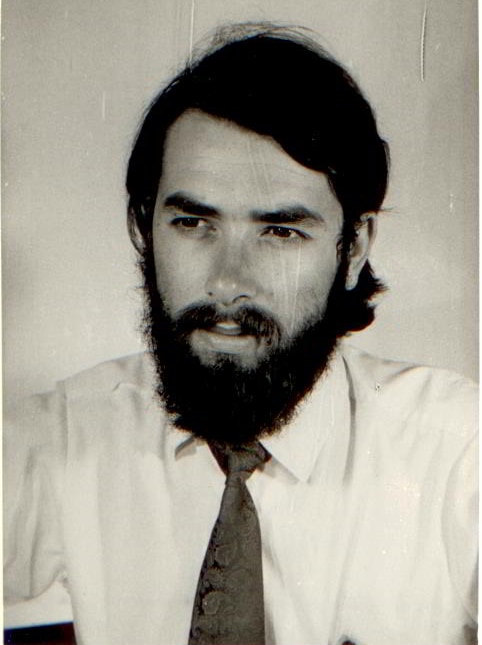 A black-and-white photo of a man with a beard wearing a shirt and tie.
