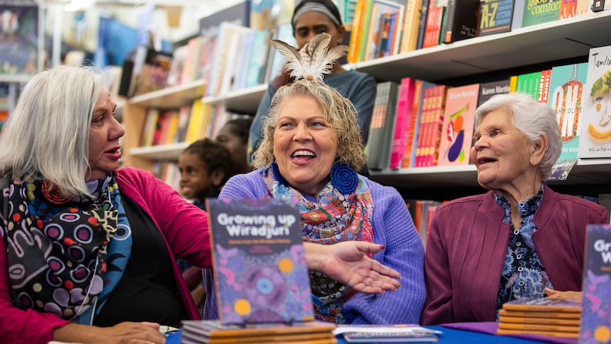 Three older Aboriginal woman sit at table with Growing Up Wiradjuri on the table