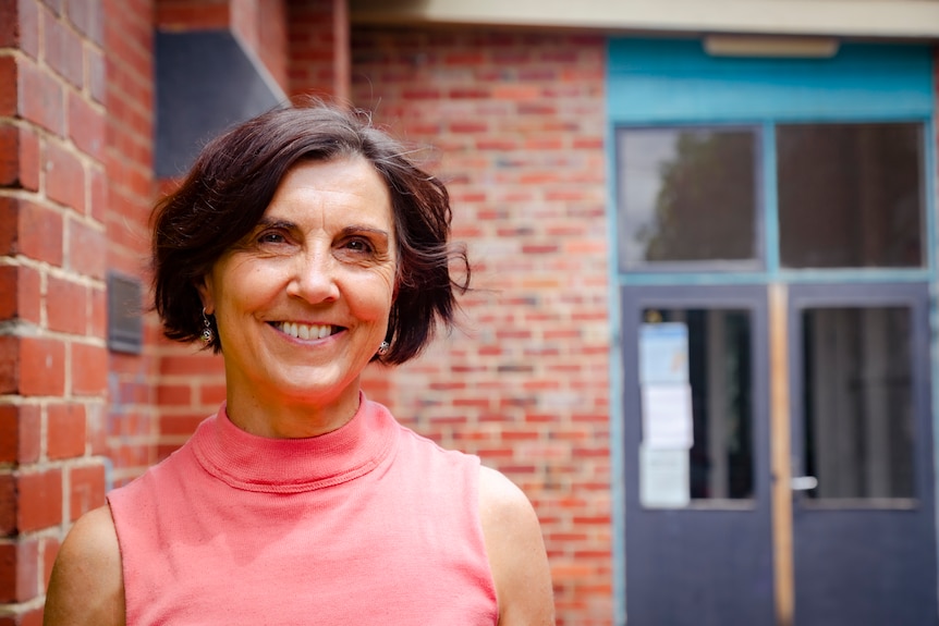 A woman with short brown hair smiles in front of a red brick building.