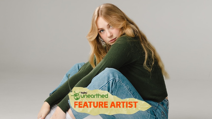 Kat Edwards, a young woman with long strawberry blonde hair, a green shirt and jeans, sits and looks toward the camera.