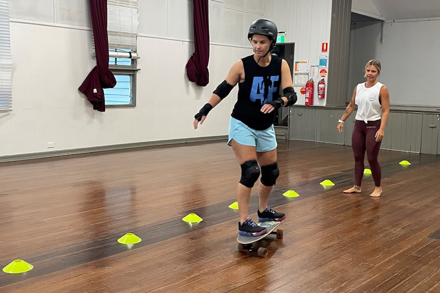 A woman skateboards through some cones in a community hall.