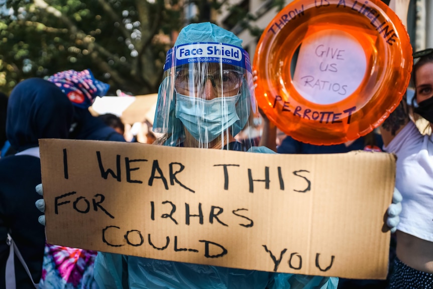 A nurse wearing PPE holding a sign