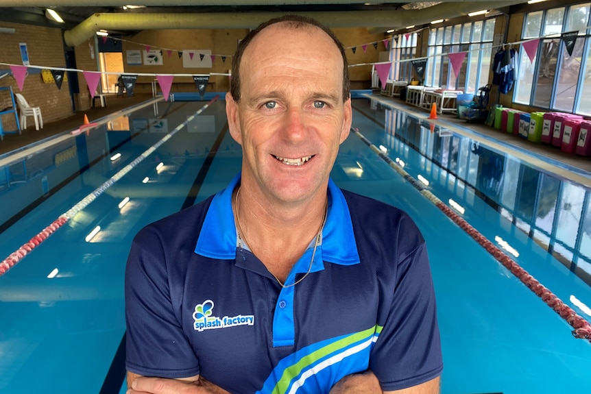 Un homme en polo souriant devant une piscine intérieure