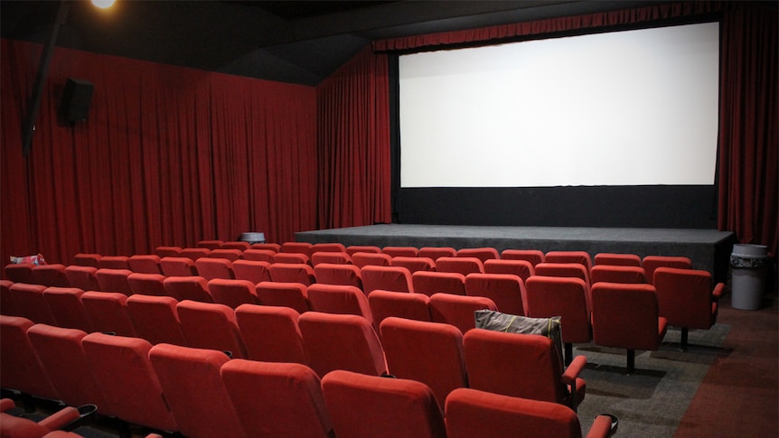 Red seats line the inside of the quaint Huskisson Pictures cinema with a white blank screen and stage at the front of the theatr