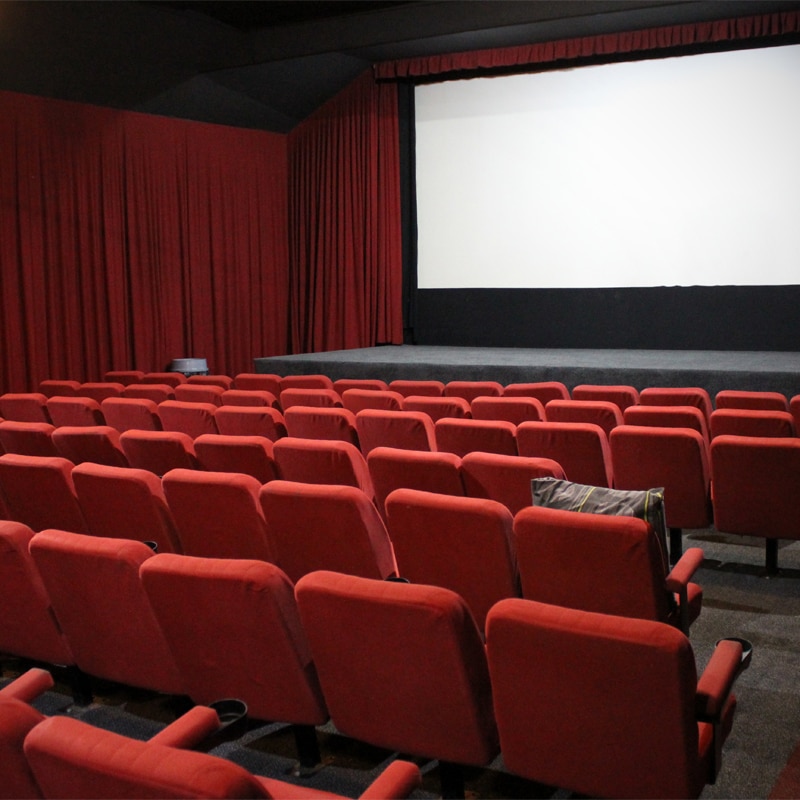 Red seats line the inside of the quaint Huskisson Pictures cinema with a white blank screen and stage at the front of the theatr