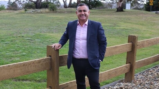 a man standing outdoors in a paddock holding onto a fence