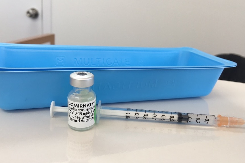 A bottle of vaccine and a needle sit in front of a blue tray