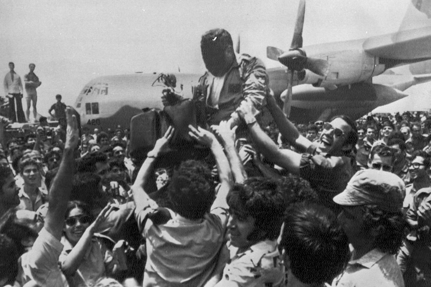 Black and white photo of man being raised above a crowd in front of a plane.