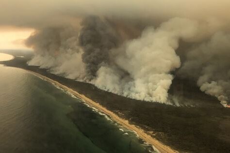 Large plumes of smoke along a coastline are seen from the air