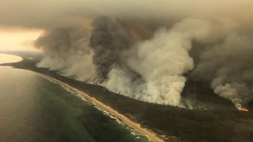 Large plumes of smoke along a coastline are seen from the air