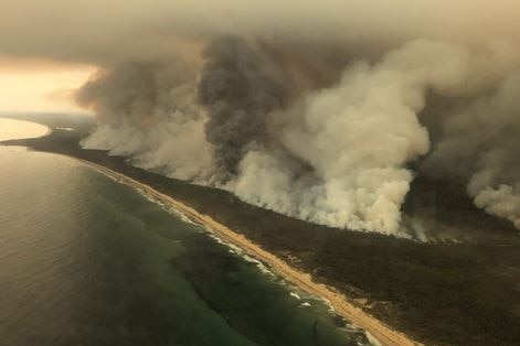 Large plumes of smoke along a coastline are seen from the air