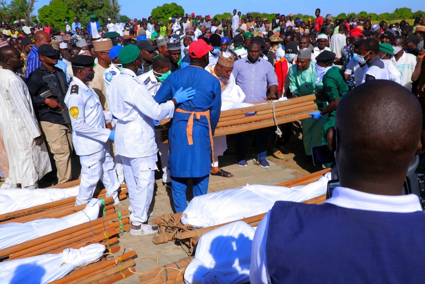 Men carry a body wrapped in white cloth surrounded by hundreds of mourners.