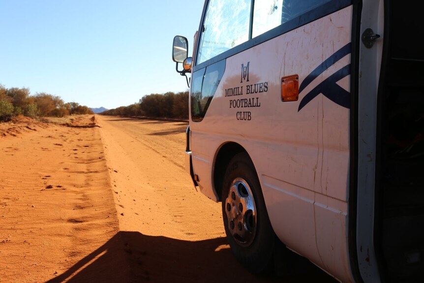 A bus stopped on the side of a red dirt road.