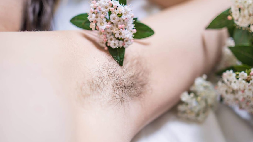 A woman's armpit with her hair grown out, and flowers scattered around.