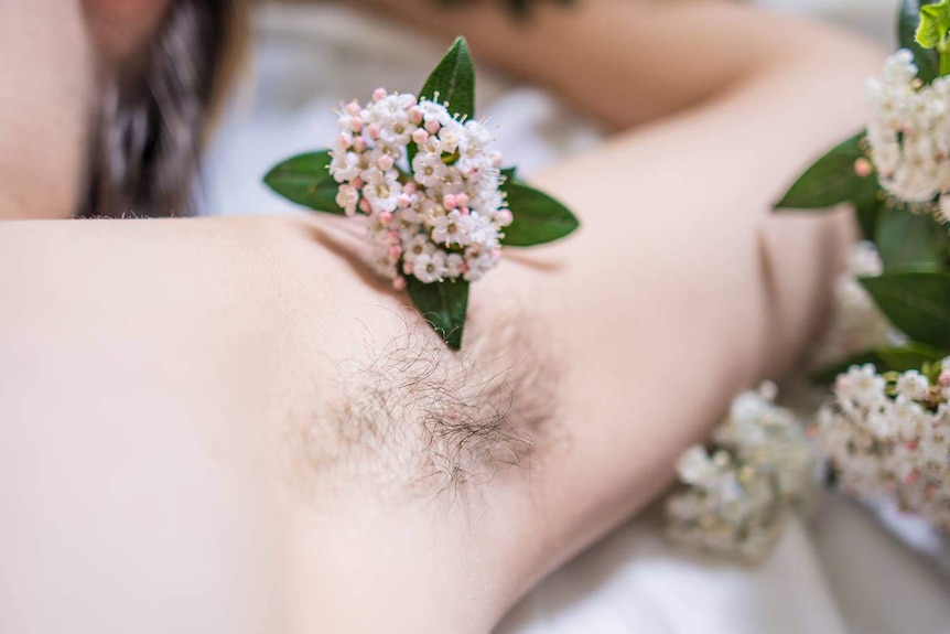 A woman's armpit with her hair grown out, and flowers scattered around.
