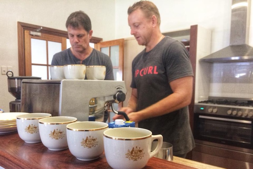 Two men stand behind coffee machine serving up coffee