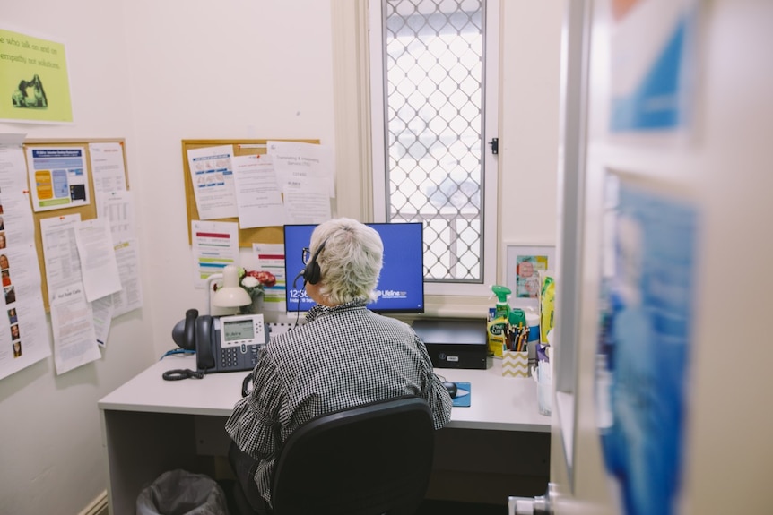 A person sits at a desk with their back to the camera and a headset on.