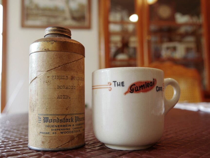 An old cannister and ceramic tea cup sit on a table.