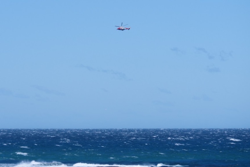 a rescue helicopter in a blue sky and choppy ocean