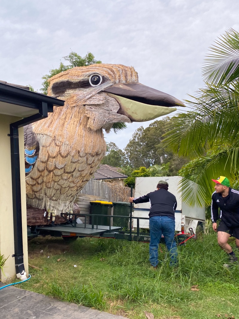 Two men moving a giant sculpture of a kookaburra.