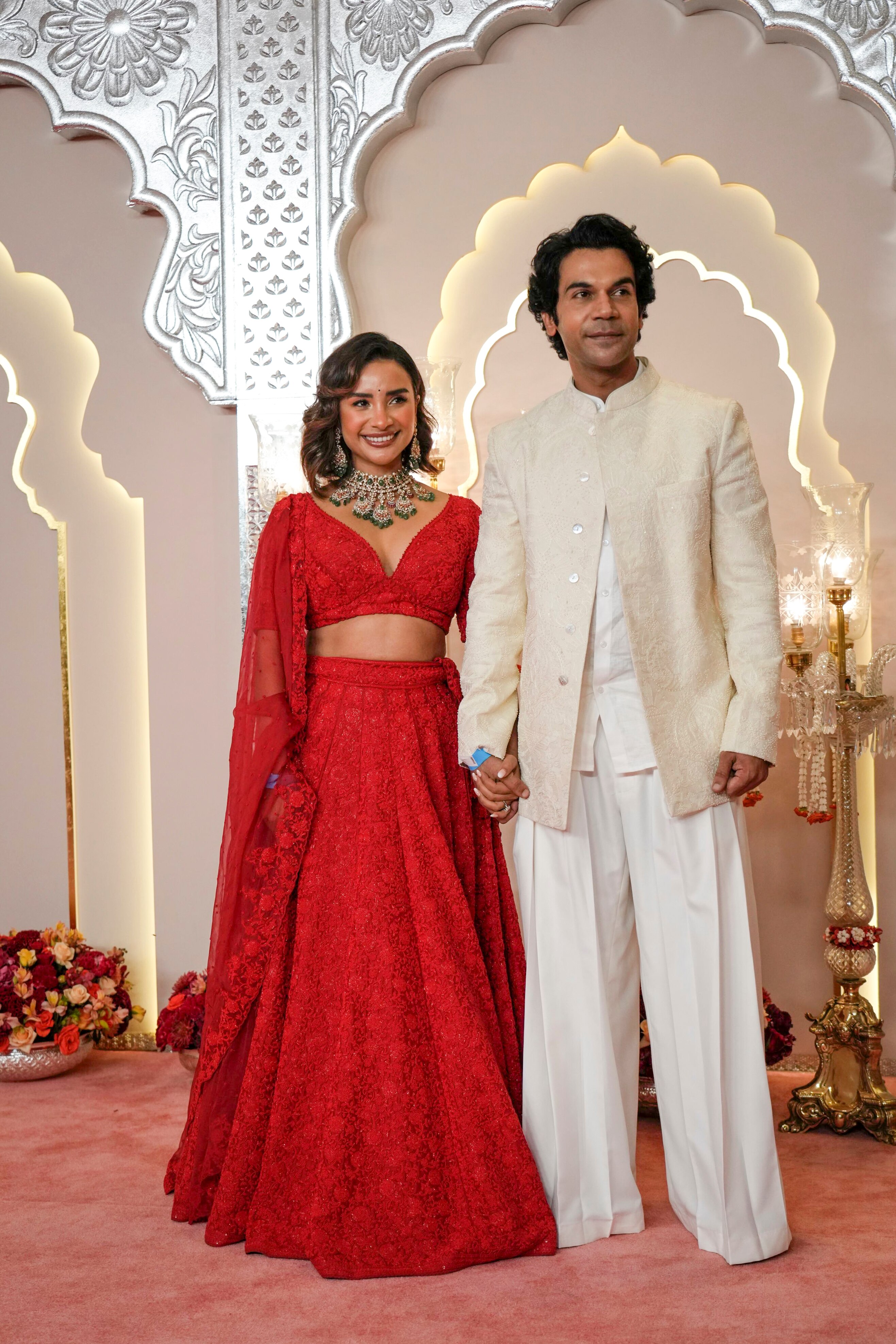 Patralekha Paul wearing a red lace skirt with a long-sleeved crop top and Rajkummar Rao wears a beige tunic and white pants