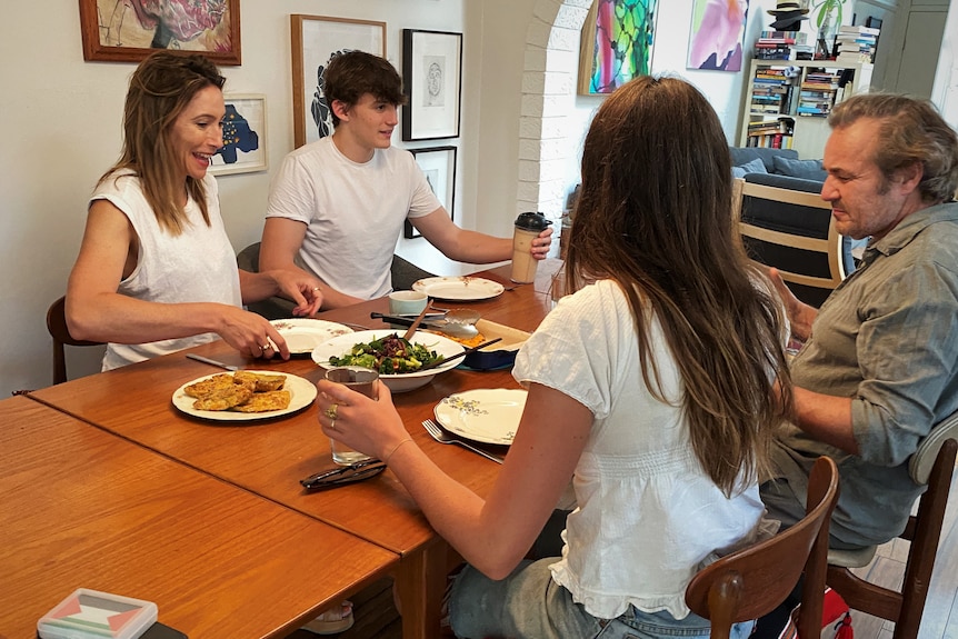 Karvan, Sparks and their two adult children sit at a dinner table eating a meal and chatting.