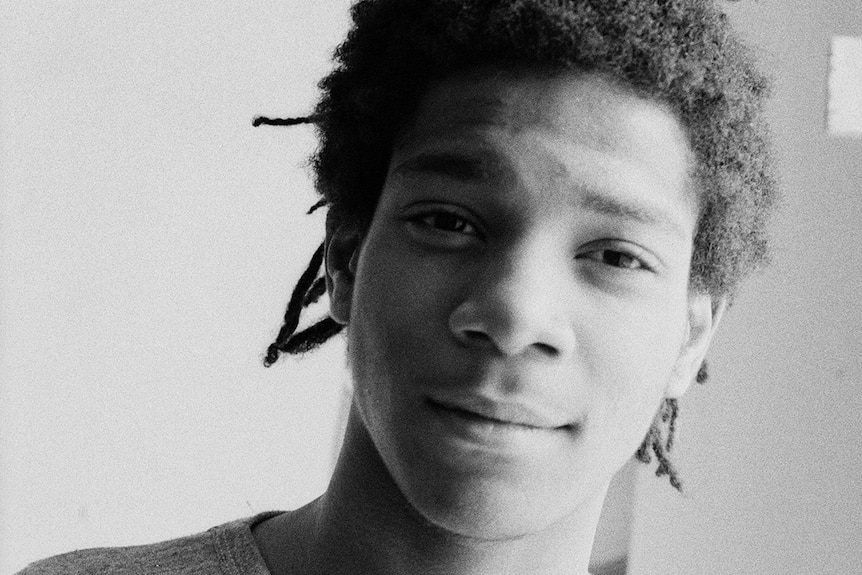 Black and white portrait of New York artist Jean-Michel Basquiat, his face half lit and half in shadow.