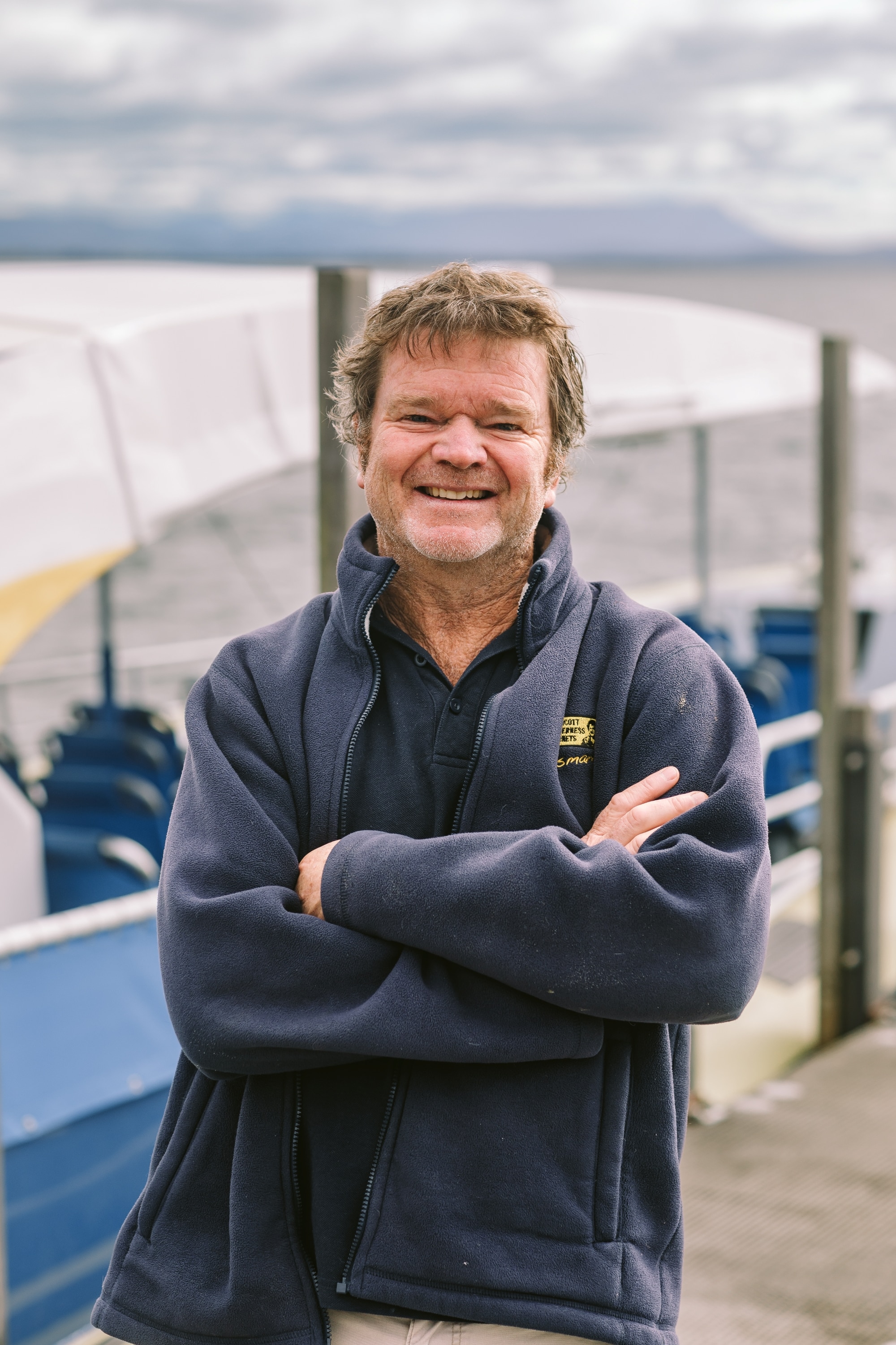 Um homem sorri para a câmera enquanto está no cais.