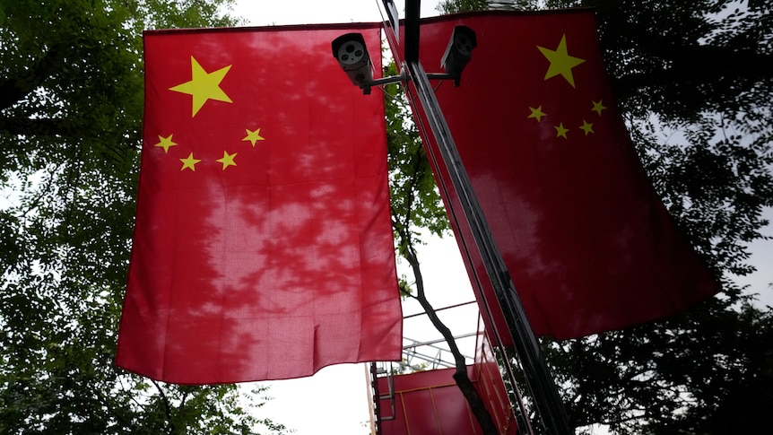 A security camera and the Chinese national flag is reflected off a glass wall 