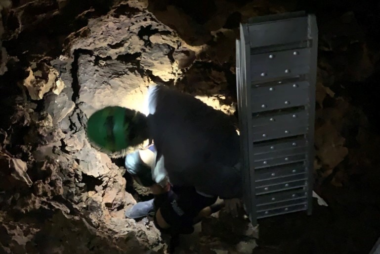 Camera crew carrying a ladder through narrow cave.