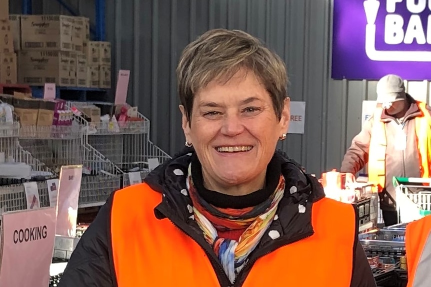Sara wears a orange foodbank vest and smiles at the camera. 