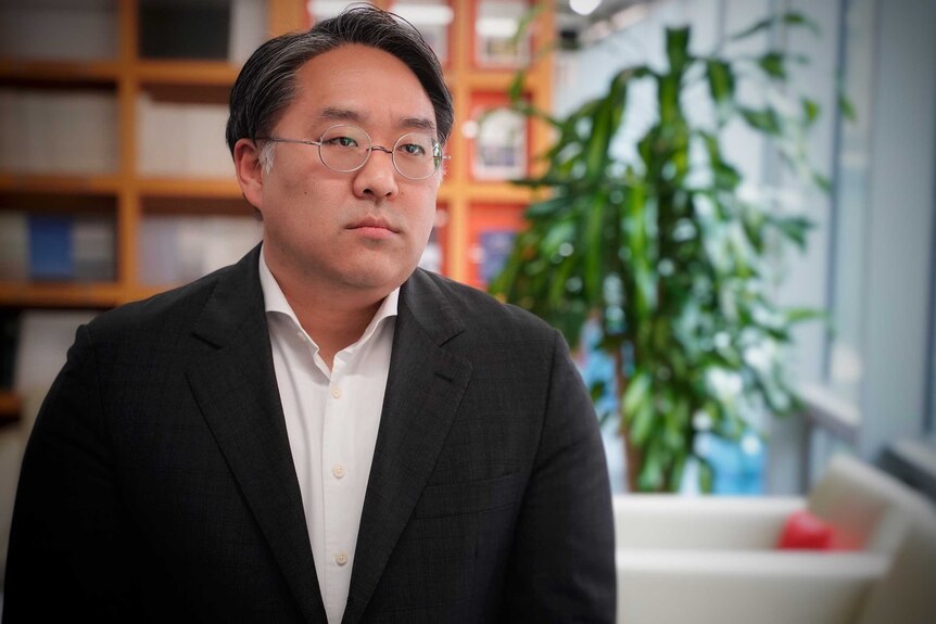 A Korean man in wire rimmed glasses looking solemn