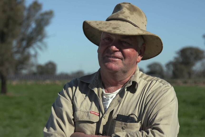 Head shot of farmer Eddie Rovers standing with arms folded in a paddock with sheep and solar panels in the background
