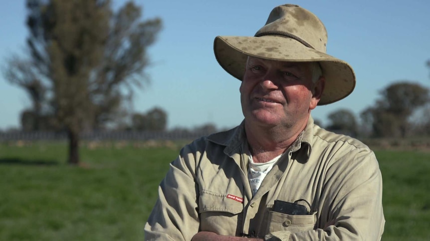 Head shot of farmer Eddie Rovers standing with arms folded in a paddock with sheep and solar panels in the background