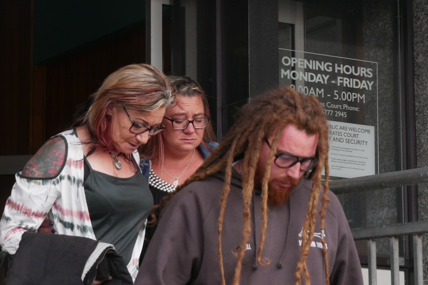 Three people leaving a court house looking emotional.