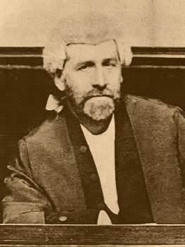 A black and white photo of a man wearing a white judge's wig and black robes.