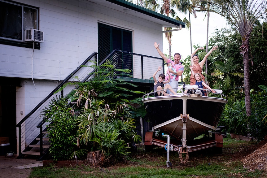 A young family pose on a boat in their front yard