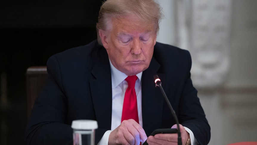 President Donald Trump looks down at his phone during a roundtable meeting.