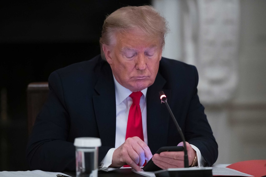 President Donald Trump looks down at his phone during a roundtable meeting.