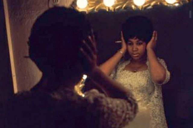 An old image of Aretha Franklin, fixing her hair in front of a mirror