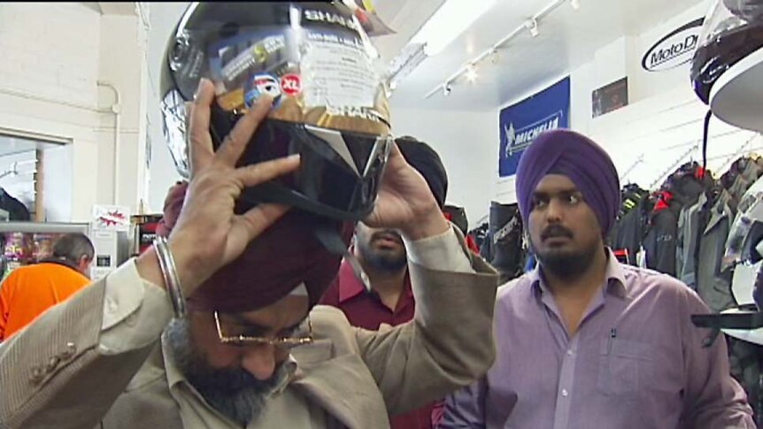 A Hobart man Harpreed Singh tries to put a helmet on over his turban.