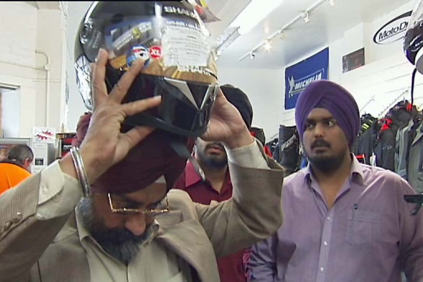 A Hobart man Harpreed Singh tries to put a helmet on over his turban.