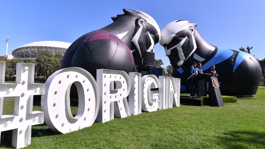 A giant "#Origin" sign stand next to maroon and blue inflatables with Adelaide Oval in background.