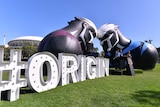A giant "#Origin" sign stand next to maroon and blue inflatables with Adelaide Oval in background.