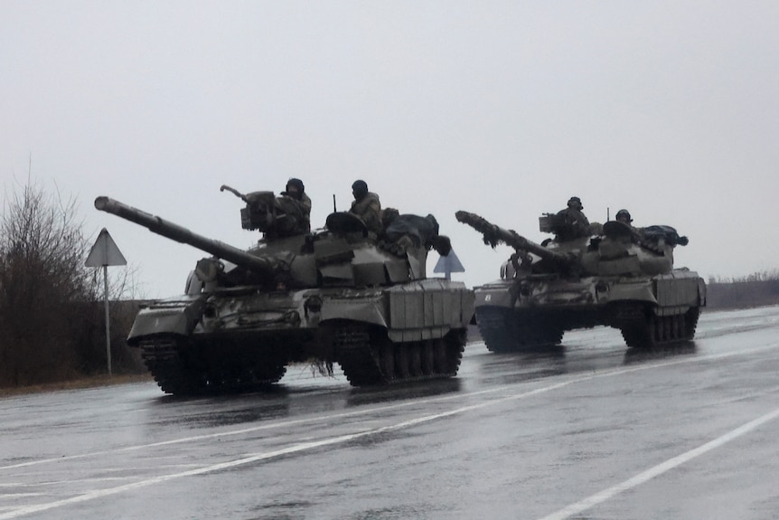 Two tanks roll down a wet street on an overcast day